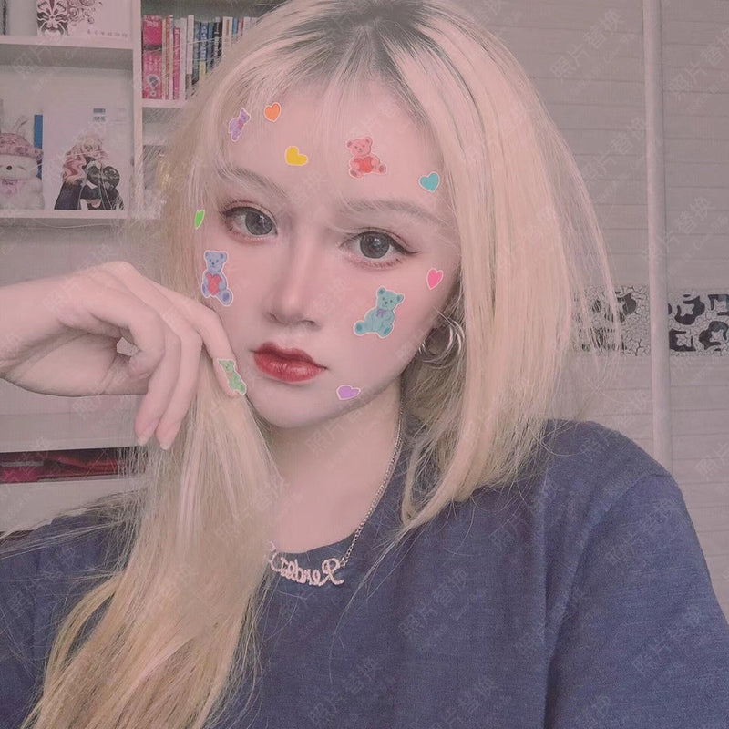 Person with blonde hair and colorful stickers on face, wearing a blue shirt.
