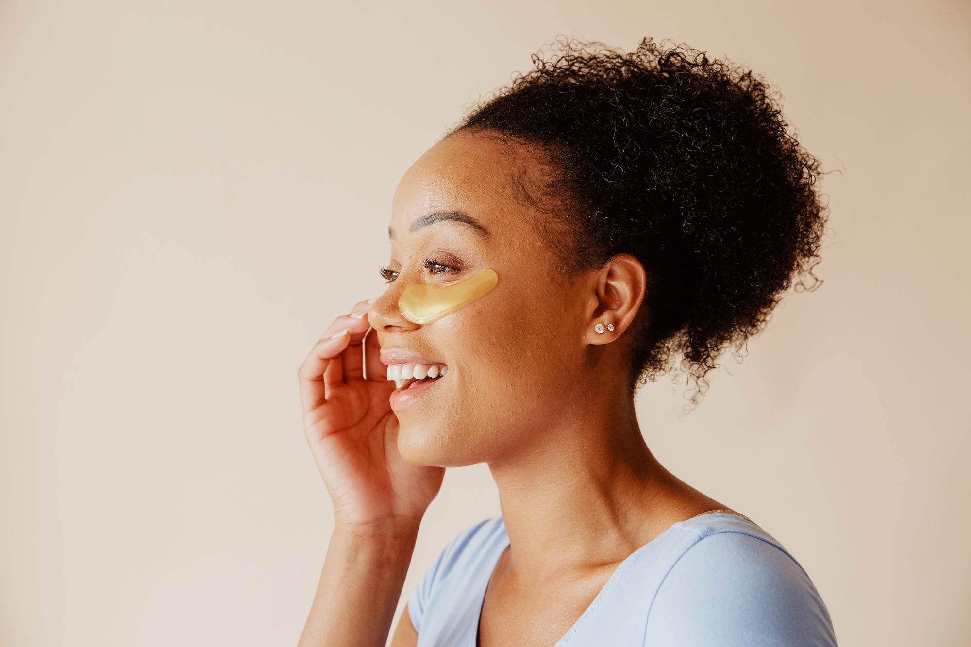 Happy woman wearing gold collagen under eye patch for skincare
